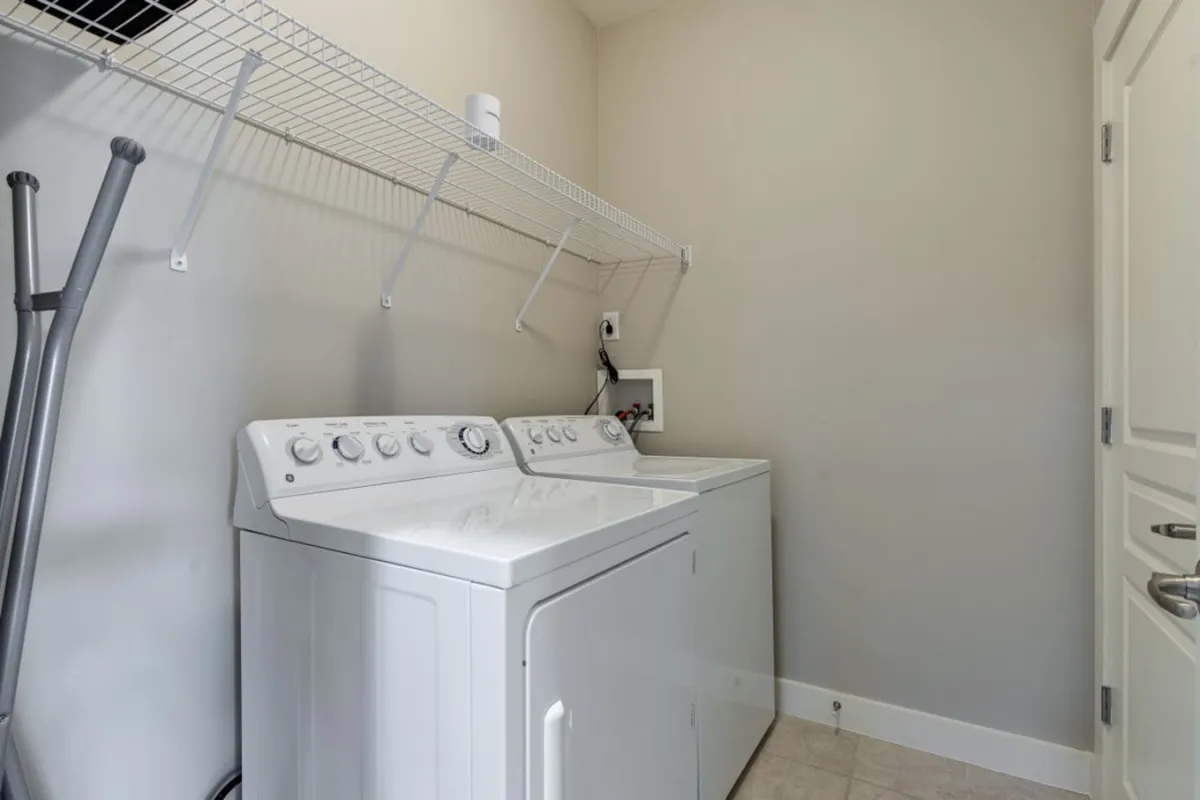 A tidy laundry area with a washing machine, drying machine, and neatly organized shelving. The efficient layout suggests that chores like laundry are easy and convenient, and the organized space feels fresh and inviting.