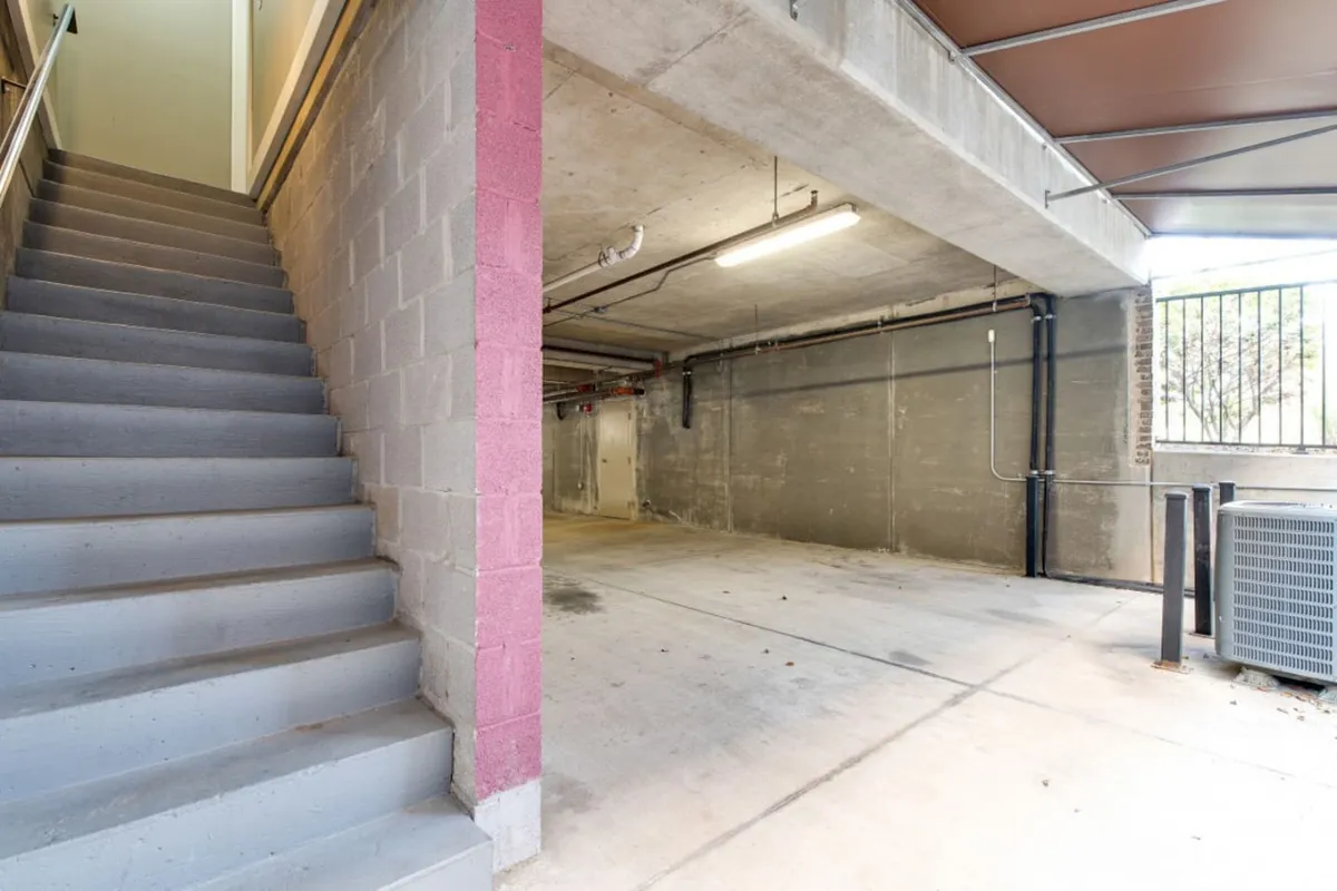 An interior garage space featuring clean concrete walls, a sturdy staircase leading to upper levels, and ample lighting. The scene demonstrates practical solutions for parking, storage, and accessing the main living areas, echoing the security and ease promised by dedicated parking.