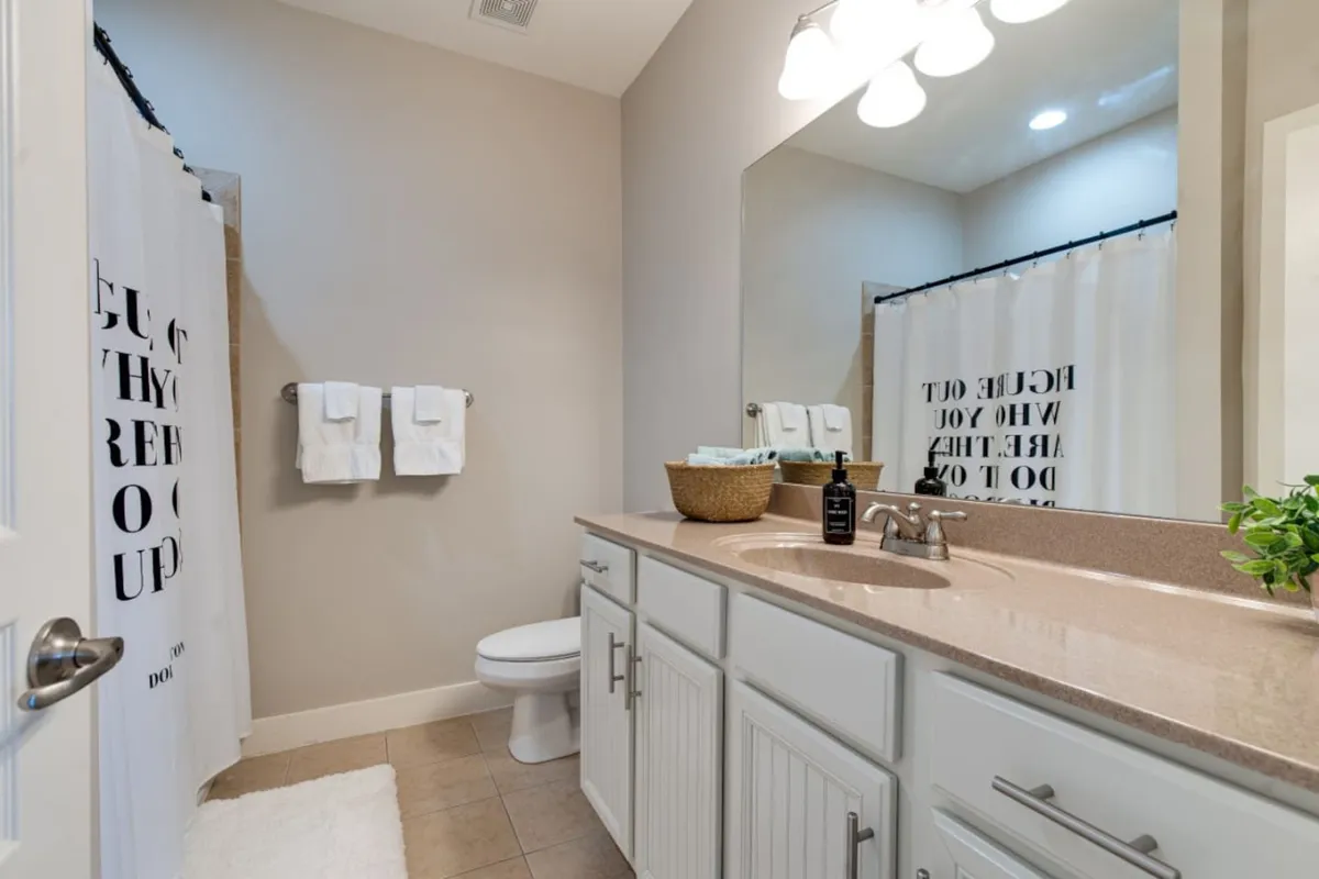 A modern bathroom with a wide vanity, large mirror, shower curtain, and neatly arranged towels, evoking a spa-like atmosphere. The space is designed for personal grooming and relaxation, supporting the 'getting ready' and self-care themes.