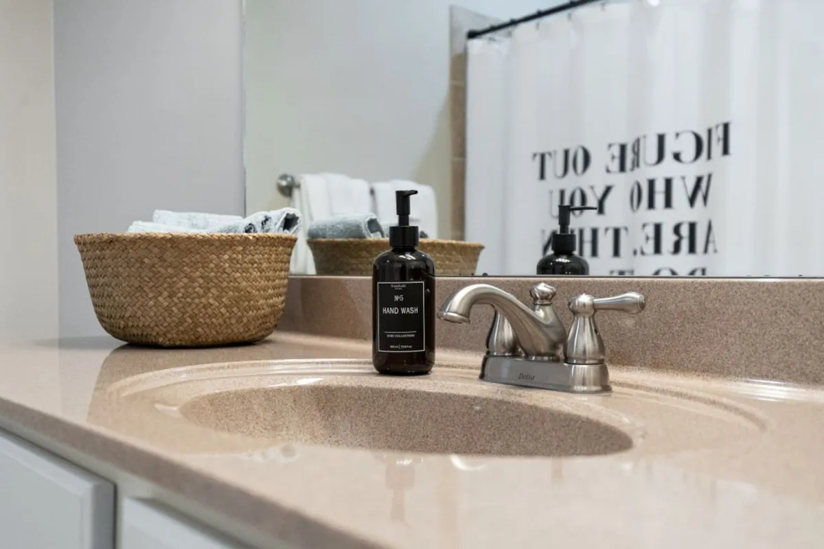 A serene bathroom sink area featuring a bottle of quality hand wash and a woven basket with towels. The mood is calm and organized, emphasizing thoughtful, green touches.
